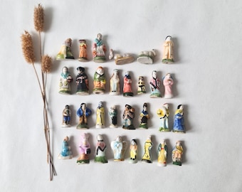May include: A collection of twenty-eight small, hand-painted ceramic figurines depicting various human figures and animals, arranged in four rows, accompanied by three dried, slender, brown botanical stalks with textured, fuzzy seed heads.