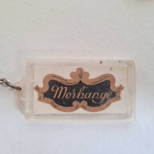 May include: A clear plastic keychain with a gold and black logo that says "Morkange".