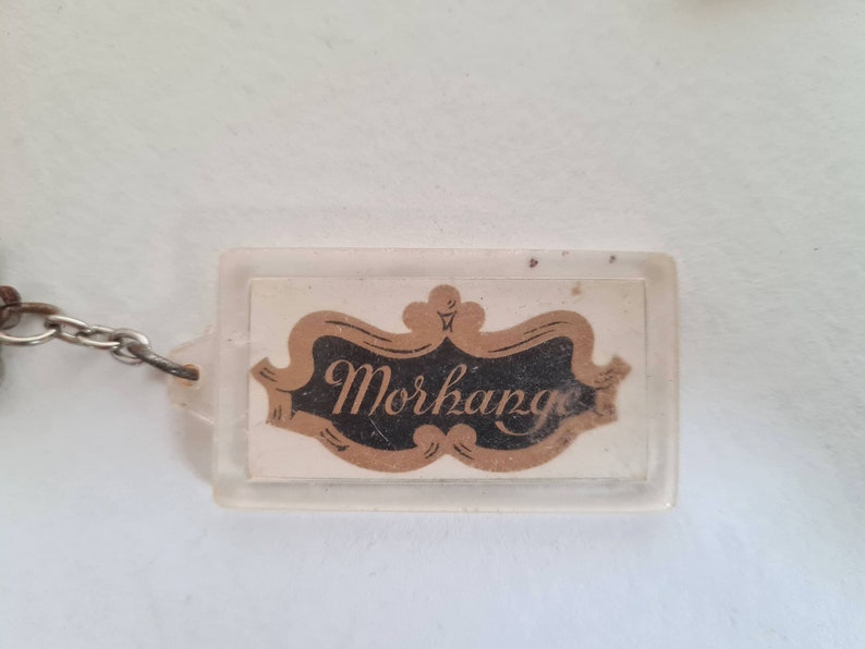 May include: A clear plastic keychain with a gold and black logo that says "Morkange".