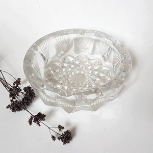 Könnte beinhalten: Ein Aschenbecher aus klarem Glas mit einem geschliffenen Glasdesign. Der Aschenbecher ist rund und hat einen gewellten Rand.