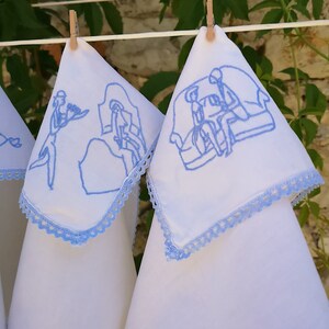 Puede incluir: Tres toallas de t&eacute; de lino blanco con dise&ntilde;os bordados en azul. Los dise&ntilde;os presentan personas en varias escenas. Las toallas tienen un borde de crochet azul.