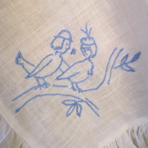 Puede incluir: P&aacute;jaros azules bordados en una rama con hojas sobre una tela de lino blanca.