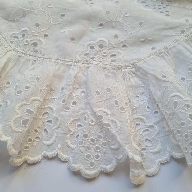 May include: White eyelet lace trim with a scalloped edge. The lace has a delicate floral pattern with small holes throughout.