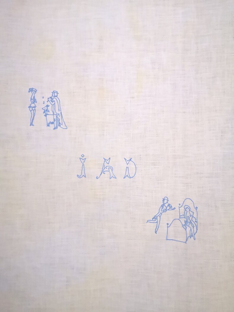 Puede incluir: Una tela de lino blanco con bordado azul de dos figuras de pie y una tercera sentada. La palabra "IAD" est&aacute; bordada en azul debajo de las figuras. La parte inferior de la tela presenta una imagen bordada azul de dos figuras en una cama.