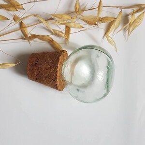 May include: A clear glass bottle with a cork stopper. The bottle is round and has a smooth surface. The cork is brown and has a rough texture.