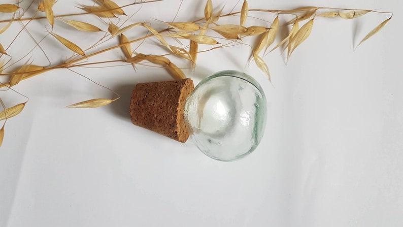 May include: A clear glass bottle with a cork stopper. The bottle is round and has a smooth surface. The cork is brown and has a rough texture.