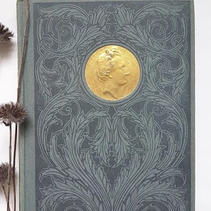 May include: A vintage book with a green cover and a gold embossed design. The design features a circular medallion with a profile of a person inside.