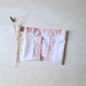 Könnte beinhalten: Weißes Baumwoll-Oberteil mit rosa Spitzenbesatz an Ausschnitt und Ärmeln. Die Spitze ist ein zartes, gewelltes Design.