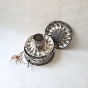 Puede incluir: Un molde para pastel de metal plateado con un centro extraíble. El molde tiene un borde acanalado y está diseñado para hacer pasteles bundt.