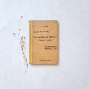 Può includere: Un libro vintage con una copertina marrone usurata e bordi ingialliti. Il titolo "Cinématique et Statique Cosmographie" è stampato in nero, insieme al nome dell'autore, "E. Jacquet". Il libro è un "Résumé Aide-Mémoire" ed è di "Librairie Hachette".