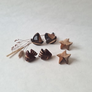 May include: A selection of handcrafted wooden ornaments. The ornaments are in the shapes of sailboats, fish, and starfish. They feature natural wood tones with dark and light brown accents. Some have a glossy finish. They are arranged on a neutral background.