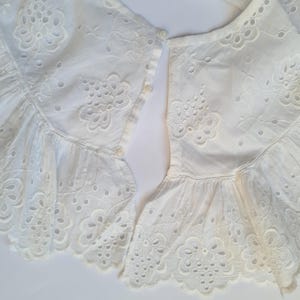May include: Two white cotton lace collars with eyelet embroidery and a button closure. The collars are ruffled and have a delicate floral design.