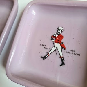 K&ouml;nnte beinhalten: Ein rosa Keramik-Aschenbecher mit einer Grafik eines Mannes in roter Jacke und Zylinder. Der Text "BORN 1820 STILL GOING STRONG" ist unter dem Mann gedruckt.