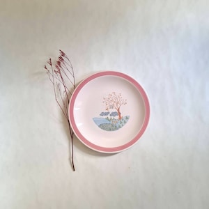 Könnte beinhalten: Ein weißer Keramikteller mit rosafarbenem Rand zeigt ein handgemaltes Design eines Baumes mit braunen Ästen und orangefarbenen Blättern, umgeben von blauen Wolken und grünem Laub. Der Teller befindet sich auf einem weißen Hintergrund.