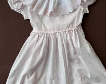 May include: A pink dress with a white lace collar and short sleeves. The dress has a smocked bodice and a full skirt.