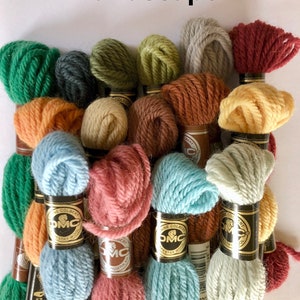 May include: A collection of skeins of embroidery floss in various shades of green, brown, orange, yellow, pink, blue, and gray. The skeins are wrapped in paper with the DMC logo and the text "The Colbert" printed on them.