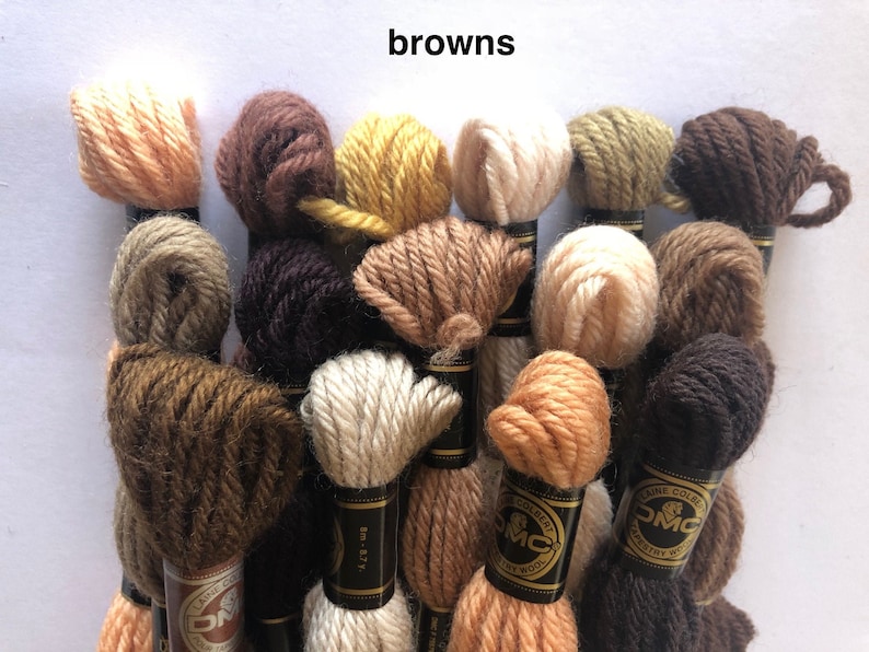 May include: A collection of 15 skeins of DMC embroidery floss in various shades of brown, beige, and cream. The skeins are arranged in a pile, with the DMC labels visible.