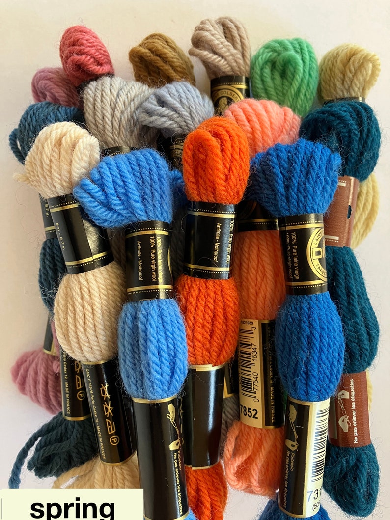 May include: A collection of 16 skeins of DMC embroidery floss in various colors, including teal, orange, blue, green, and beige. The skeins are wrapped in black and gold packaging with the DMC logo and the text "100% Pure Virgin Wool" and "Antimite-Mothproof".
