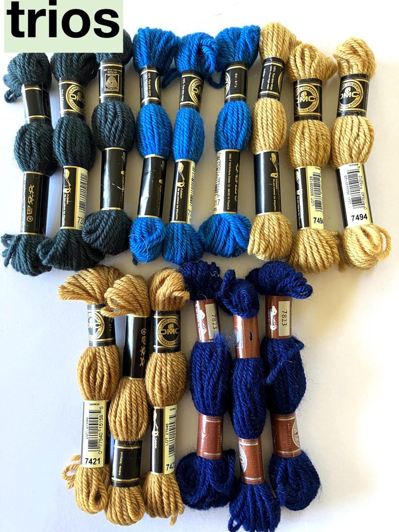 May include: A collection of DMC embroidery floss spools in various colors, including dark green, blue, and gold. The spools are labeled with the DMC numbers 7421, 7494, 7823, and 7317.