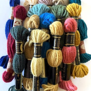 May include: A collection of DMC embroidery floss spools in various colors, including red, blue, green, yellow, and brown. The spools are labeled with the DMC color number and the text "100% Pure laine vierge" and "100% Pure virgin wool".