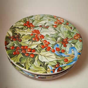 May include: A stack of ceramic plates with a festive holly and berry design. The plates feature green leaves, red berries, and blue ribbon accents, perfect for holiday dining. The plates are round and have a glossy finish.