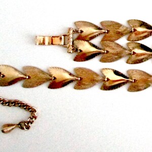 May include: A gold-tone bracelet made of linked heart-shaped charms. The bracelet is made of two rows of charms, with a clasp on one end and a chain on the other.