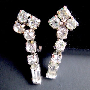 May include: A pair of silver tone clip-on earrings with a row of clear rhinestones in a curved shape.