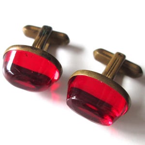 May include: A pair of cufflinks with red glass insets and gold-toned metal accents.