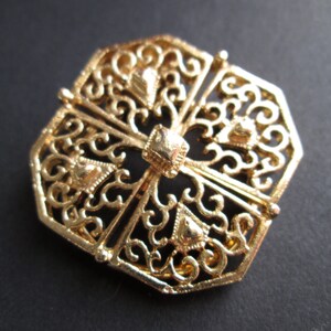 May include: A gold-toned filigree brooch with a geometric octagonal shape and intricate floral designs.