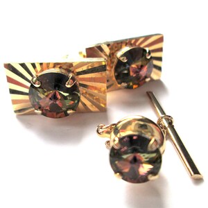 May include: A set of gold cufflinks and a tie tack with a sunburst design and a round, multi-colored gemstone in the center.