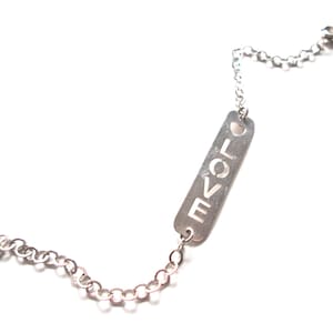 May include: Silver bracelet with a rectangular charm spelling out "LOVE". The charm is linked to a fine chain with a lobster clasp. A small heart shape is cut out at the top of the charm. The bracelet is made of silver.