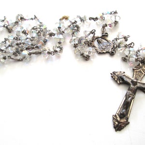 以下が含まれることがあります： クリスタルビーズのチェーンとシルバーの十字架が付いたシルバーのロザリオ。十字架にはイエス・キリストの像が描かれています。