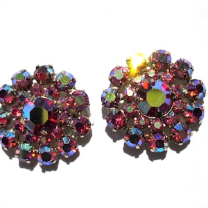 May include: A pair of iridescent red and purple flower-shaped earrings with rhinestones.