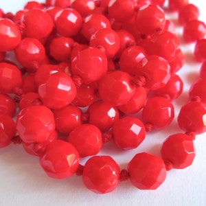 May include: A long strand of bright red faceted beads strung on a red cord. The beads are round and have a slightly irregular shape.