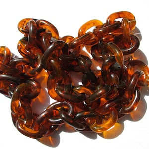 May include: A long chain of amber-coloured plastic links. The links are thick and rounded, and the chain is lying in a loose pile on a white surface.
