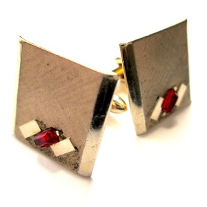 May include: A pair of silver cufflinks with a geometric design and red gemstone accents.