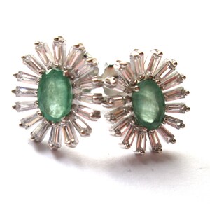 May include: A pair of silver earrings featuring green oval gemstones surrounded by a halo of smaller clear stones.