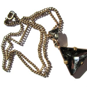 May include: A gold chain necklace with a large, faceted, triangular pendant made of clear glass. The pendant has a gold setting.