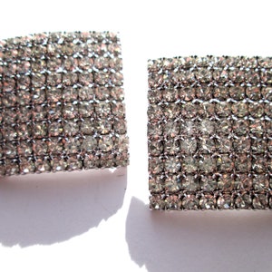 May include: A pair of silver tone square earrings with clear rhinestones.