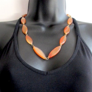Peut inclure: Un collier composé de perles de cornaline orange avec des connecteurs en métal doré. Les perles sont de forme ovale et ont une finition lisse et polie.