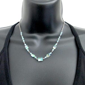 Peut inclure: Un collier en chaîne argent avec des perles de verre rectangulaires et rondes bleu clair.