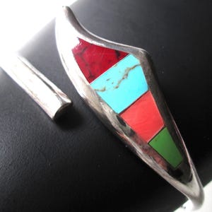 May include: A silver bracelet with a geometric design inlaid with turquoise, red, and green stones.