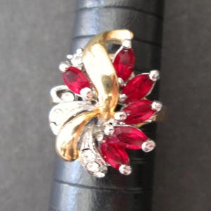 May include: A gold and silver ring featuring a cluster of red and clear rhinestones in a flower design.