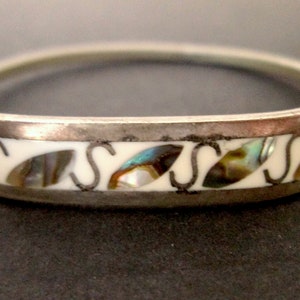 Peut inclure: Un bracelet en argent avec un incrustation blanche et un motif de lettres 'S' alternées et de morceaux d'ormeau iridescent.