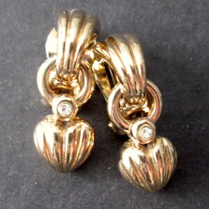 May include: Gold tone clip-on earrings with a heart-shaped design and a single clear rhinestone on each earring.