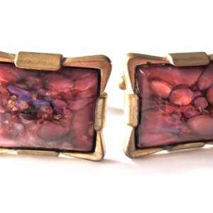 Peut inclure: Une paire de boutons de manchette avec un motif carré marbré rose et violet serti dans un cadre en métal doré.