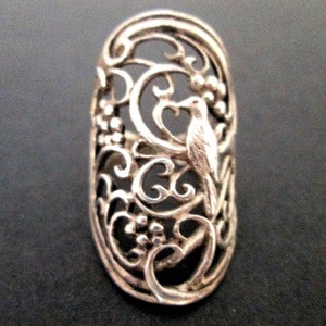 May include: A silver ring with a delicate filigree design featuring a bird perched on a branch. The ring is open and adjustable.