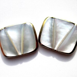 May include: A pair of square-shaped earrings with a white mother-of-pearl inlay and a gold-toned metal frame.