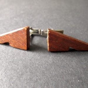May include: A pair of wooden cufflinks with a triangular shape. The cufflinks are made of dark brown wood and have a silver metal clasp.