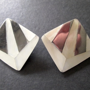 May include: A pair of square-shaped earrings with a white and silver geometric design. The earrings are made of mother of pearl and have a shiny finish.